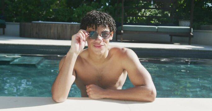 Portrait of happy biracial man with sunglasses at pool in garden on sunny day