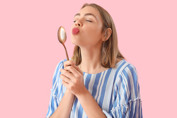 Young woman with golden spoon blowing kiss on pink background