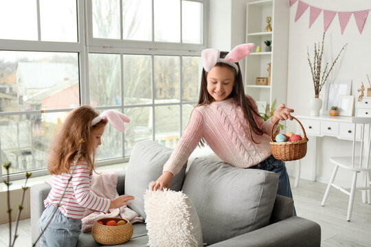 Little girls in bunny ears with baskets of Easter eggs at home