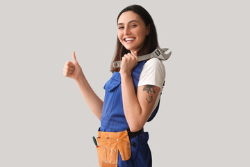 Female plumber with wrench showing thumb-up on grey background