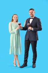Young man in suit giving his wife glass of wine on blue background