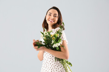 Young woman in dress with alstroemeria flowers on grey background