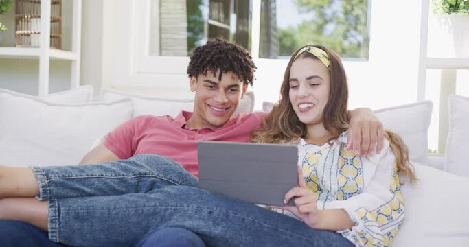 Happy biracial couple spending time at home together using laptop and smartphone