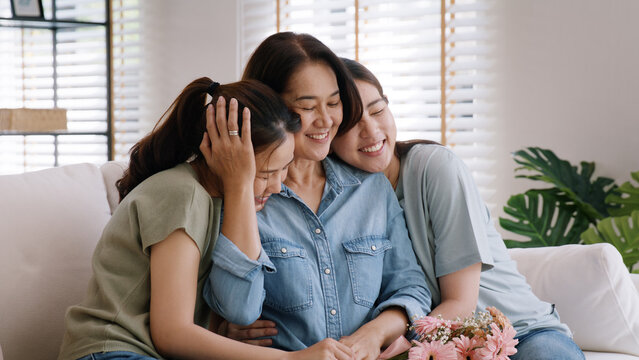 Happy time May Mother day cuddle hug care love face to face kiss cheek to mature mum. Asia middle aged old mom adult people smile enjoy receive gift flower from young child sitting at home sofa relax.
