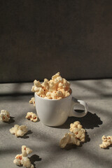 Popcorn in white cup under sunlight with shadow on grey background. Cinema snacks. Party time.