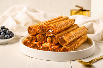 Plate of delicious wafer rolls with boiled condensed milk on white wooden table, closeup