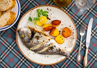Delicious grilled gilthead bream (dorada) served with baked potatoes, slice of lemon and fresh greens