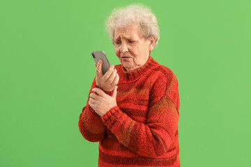 Sad senior woman with mobile phone on green background