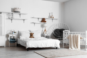 Interior of light bedroom with bed, baby crib and armchair