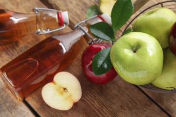 Glass bottles of fresh apple cider vinegar and fruits on wooden background