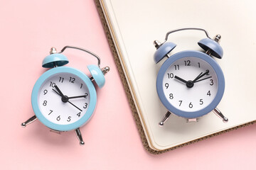Alarm clocks and notebook on pink background, closeup