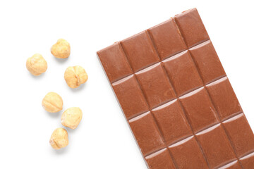 Tasty chocolate bar and hazelnuts on white background, closeup