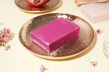 Golden plate with natural soap bar and flowers on color background