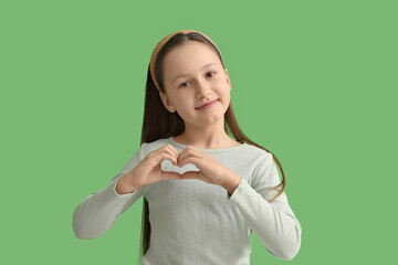 Cute little girl making heart with her hands on green background