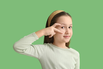 Cute little girl making heart with her hand on green background, closeup