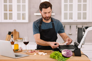 Man making dinner while watching online cooking course via laptop in kitchen