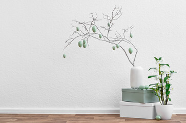 Vase with tree branch, Easter eggs and houseplant near light wall