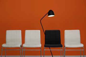 White chairs with black one and lamp near orange wall. Recruiter searching employee