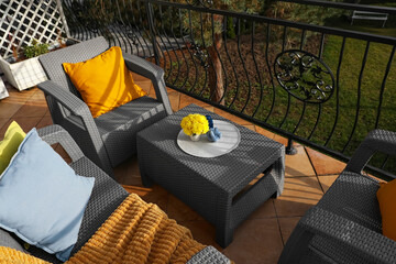 Colorful pillows, soft blanket and yellow chrysanthemum flowers on rattan garden furniture outdoors