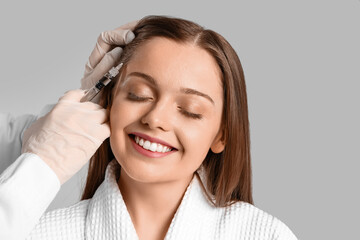 Woman with hair loss problem receiving injection on  light background
