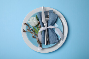 Festive table setting with willow twigs and tulip on light blue background, top view. Easter...