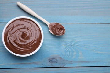 Bowl and spoon with tasty chocolate paste on light blue wooden table, flat lay. Space for text