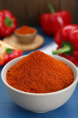 Bowl with aromatic paprika powder and fresh bell peppers on blue wooden table