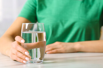 Healthy habit. Woman with glass of fresh water at white table, closeup