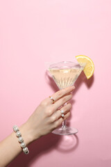 Woman holding martini glass of refreshing cocktail with lemon slice on pink background, closeup