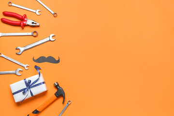 Paper mustache with work tools and gift on orange background. Father's Day celebration