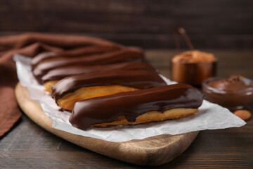 Delicious eclairs covered with chocolate on wooden table, closeup