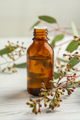 Bottle of eucalyptus essential oil and leaves on white wooden table