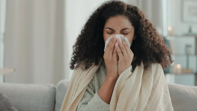 Sick, home and woman in a home living room with illness and blowing nose with a tissue. Sofa, lounge and sinus problem of a mixed race female with allergies, flu and sneezing issue in a house