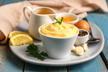 Bowl with tasty mayonnaise sauce and ingredients on color wooden table