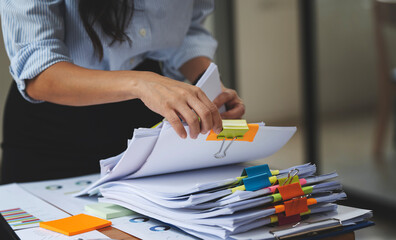 Businesswoman hands working in Stacks of paper files for searching and checking unfinished document achieves on folders papers.