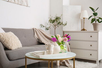Vase with hyacinth flowers, teapot and cups on coffee table in living room