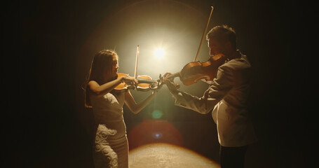 Duet of two professional violin players having a solo together, performing on stage during concert, spotted by light on black background  © andreybiling
