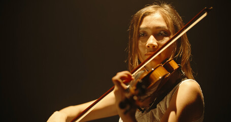 Experienced asian female violin player having a solo during the concert, spotted by light on black background  © andreybiling