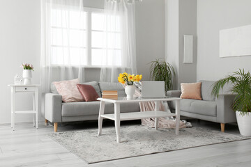 Interior of living room with modern laptop and flower vase on coffee table near sofas