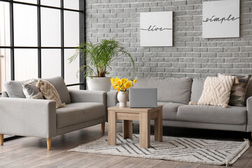 Interior of stylish living room with modern laptop and flower vase on coffee table