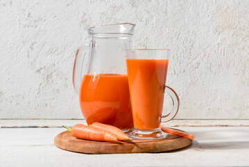 Fototapeta Glass and jug of fresh carrot juice on white grunge table obraz
