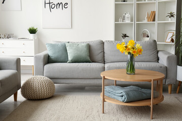 Interior of modern living room with cozy grey sofa and flower vase on coffee table