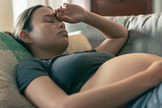 A depressed pregnant woman resting at home alone, stressed and nauseous.
