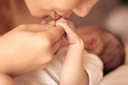 A mother kissing and holding hand the hand of her newborn baby.
