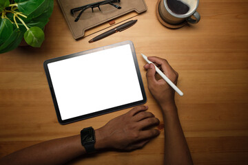 Above view of creative man hand holding stylus pen and using digital tablet on wooden working desk.