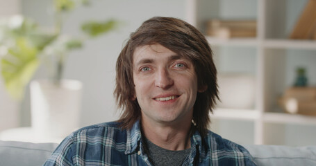 Head shot happy young 30s handsome caucasian man sitting on sofa, looking at camera, involved in web camera conversation with family or friends, enjoying video call distant communication at home.