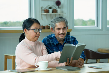 wife is inviting husband looks the contents of a book, active senior couple spend time together for reading a book, concept of family,relationship,activity,hobbies,relaxing