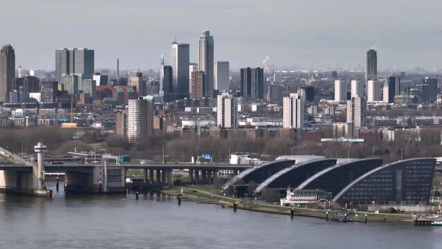 Wide aerial panning shot of the Rotterdam skyline with the Van Brienenoord bridge over the Nieuwe Maas, and vehicle traffic 