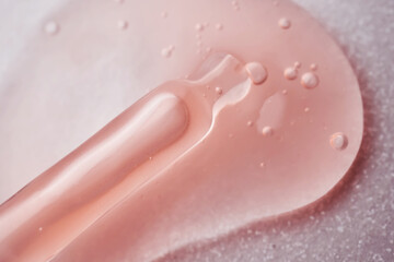 A pipette with a viscous pink cosmetic lies in a drop.