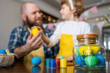 Easter Family traditions. Father and caucasian happy child with bunny ears dye and decorate eggs with paints for holidays while sitting together at home table having fun. Negative space